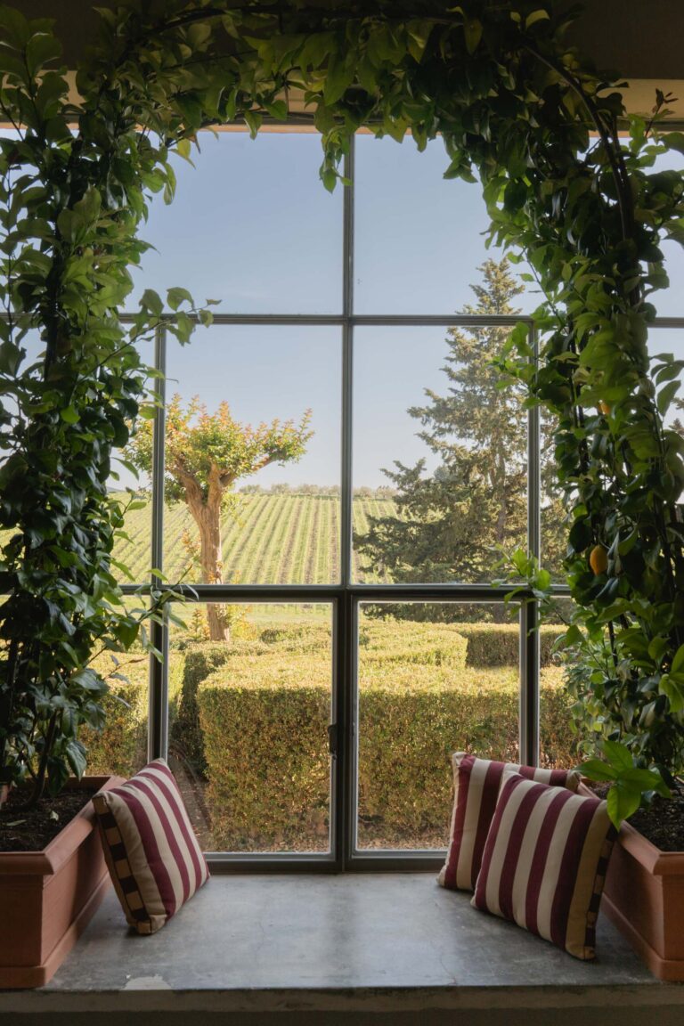 Vetrata della Limonaia di Casa Ruffino con seduta, cuscini a righe e vista sui vigneti e le siepi della tenuta