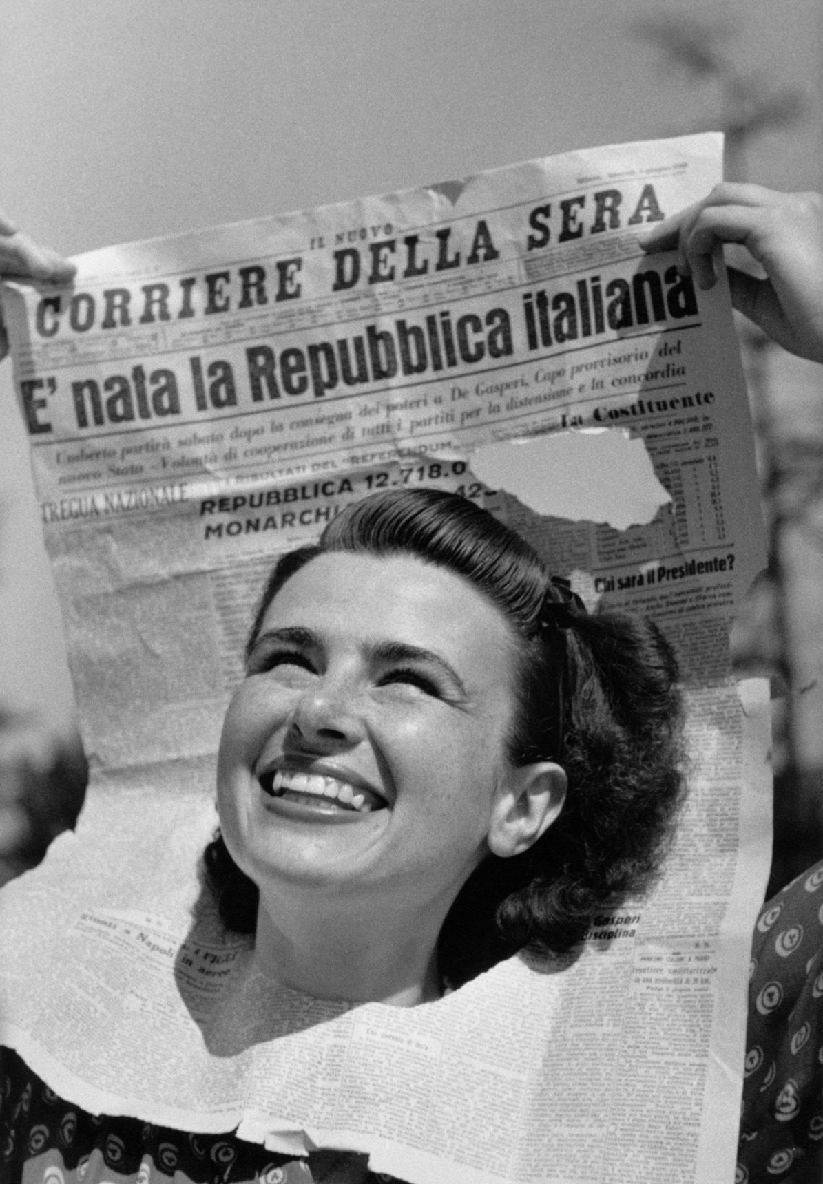 Anna Iberti sorride col volto dentro una prima pagina del Corriere della Sera che titola “È nata la Repubblica italiana”