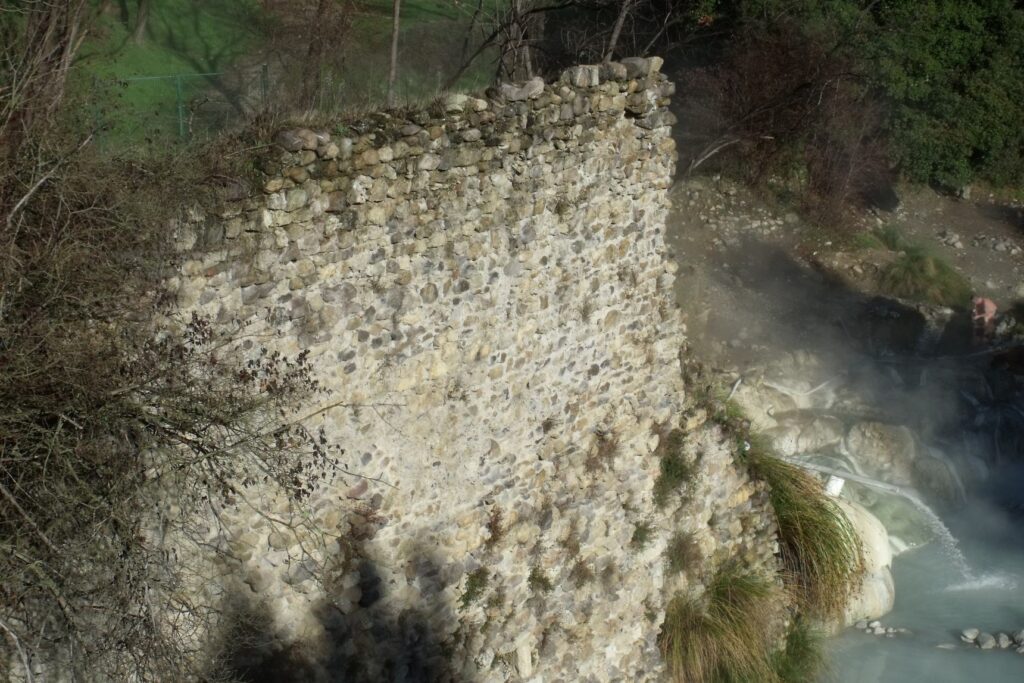 Le mura in pietra delle antiche terme fortificate di Petriolo e l'acqua sulfurea che fuma scendendo verso il Farma