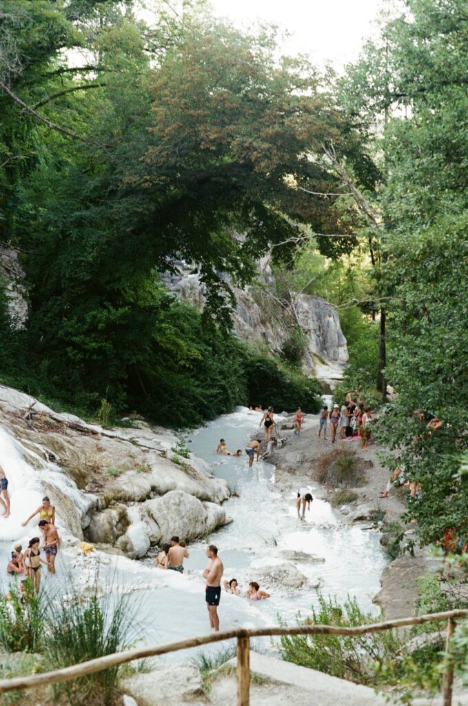 Le cascate bianche di calcare di Bagni San Filippo nel bosco, con alcuni bagnanti nelle vasche d'acqua termale