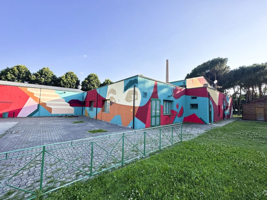Il murale astratto di Wallscape a Bibbiena: forme rosse, azzurre, gialle e rosa dipinte su tutto un edificio basso