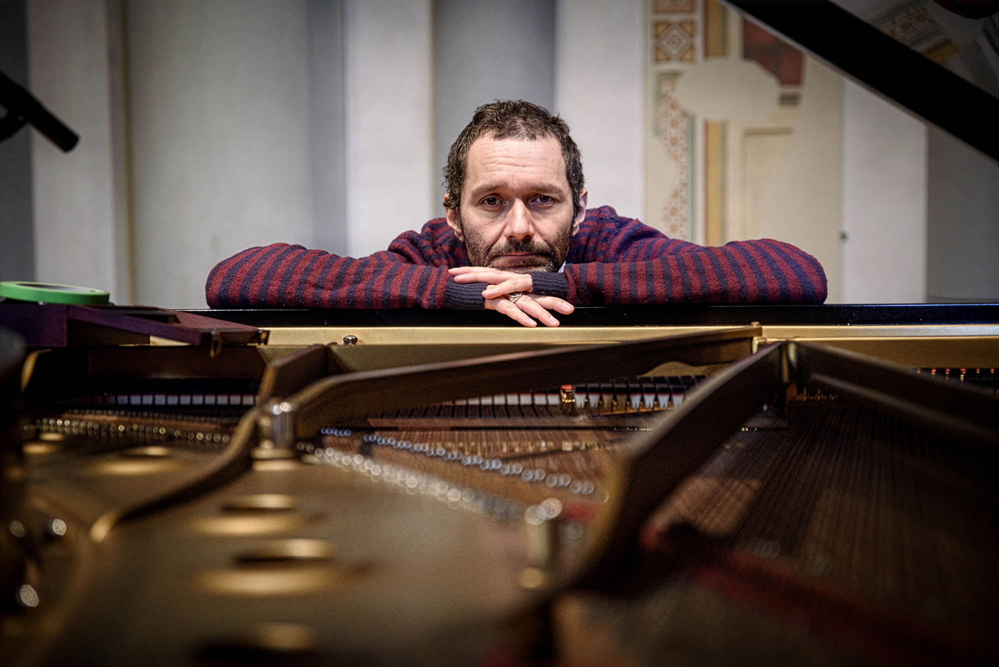 Davide Boosta Dileo appoggiato al telaio di un pianoforte a coda aperto, in una sala dalle pareti chiare