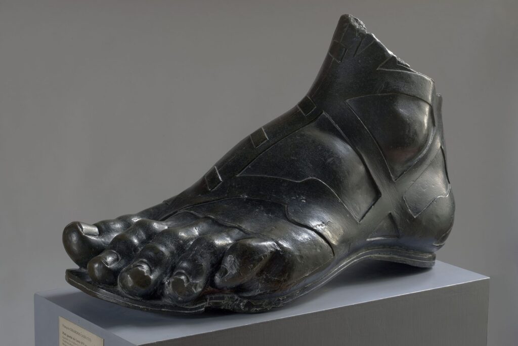 Il grande piede sinistro in bronzo scuro della statua equestre di re Luigi XIV, appoggiato su un basamento chiaro