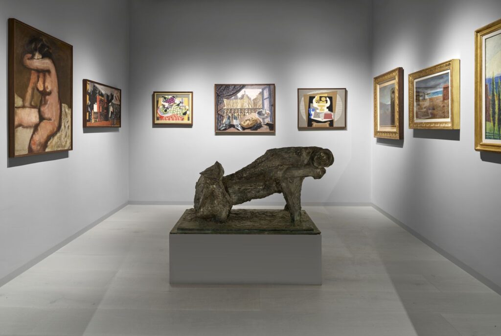 Una sala con una scultura scura distesa al centro, su un basamento, e dipinti in cornici dorate alle pareti
