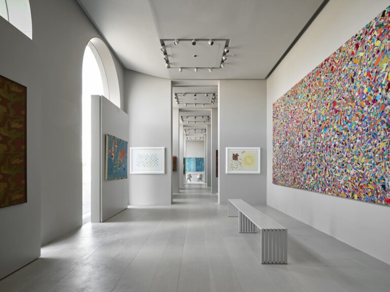 Una sala di Palazzo San Giorgio con finestra ad arco, una grande opera multicolore alla parete e la fuga delle sale