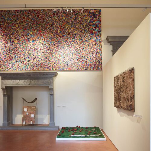 Sala con camino in pietra serena sormontato da una grande tela multicolore e due installazioni a terra sul pavimento in cotto