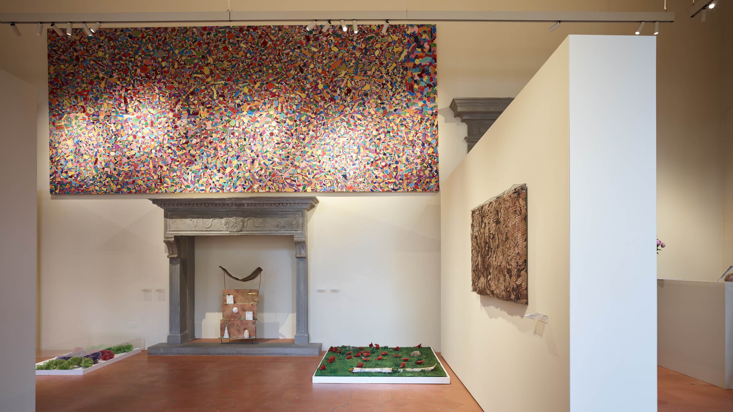 Sala con camino in pietra serena sormontato da una grande tela multicolore e due installazioni a terra sul pavimento in cotto