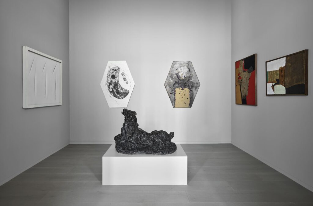 Una sala della Collezione Casamonti: una scultura scura su basamento bianco, due opere esagonali e quadri alle pareti