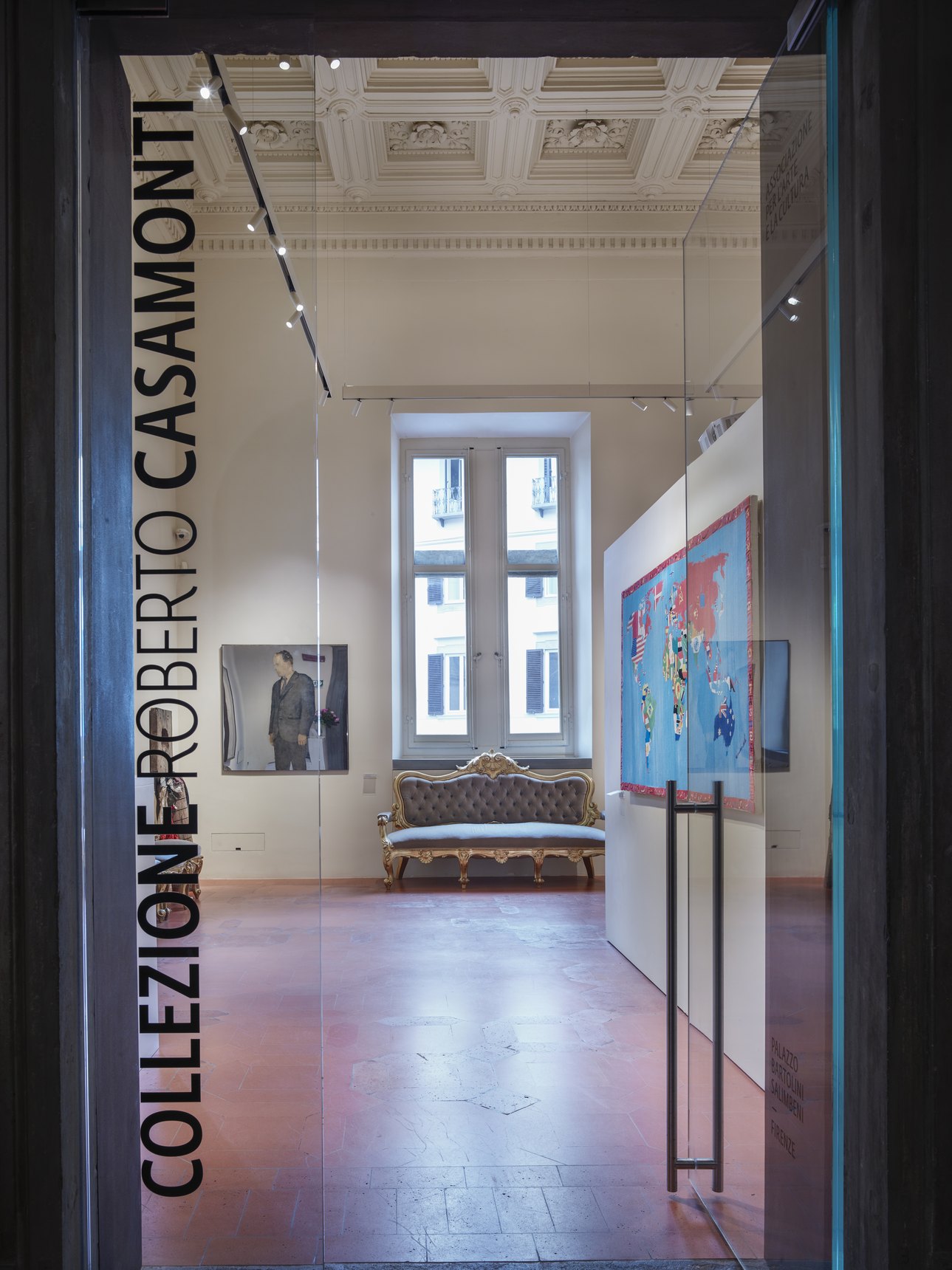 Vetrata d'ingresso con la scritta verticale Collezione Roberto Casamonti e, oltre il vetro, una sala con divano e finestra
