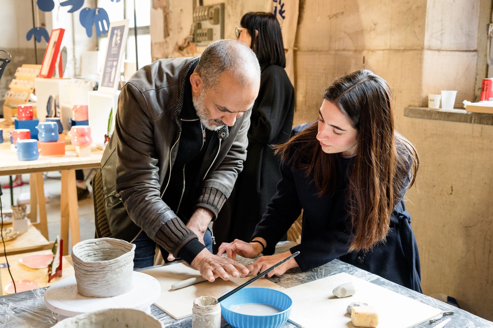 Due persone modellano l’argilla su un tavolo da lavoro durante un workshop di ceramica, fra stampi e ciotole