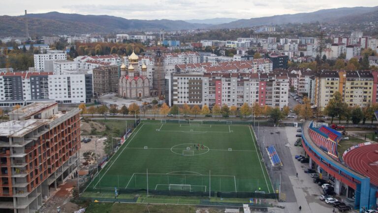 Il campo d'allenamento dell'FK Borac visto dall'alto, fra palazzi, un cantiere e una chiesa dalle cupole dorate