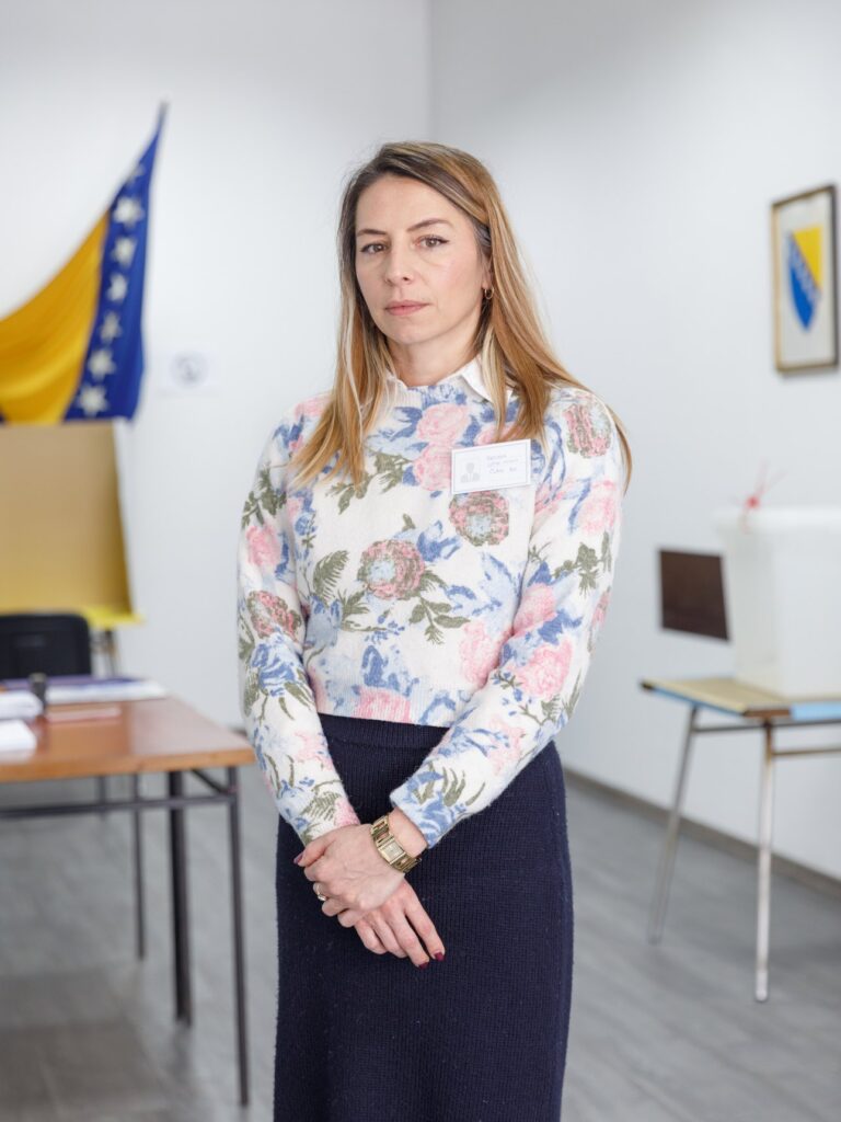 Belma Lepir-Cviko in piedi in un seggio elettorale di Novo Sarajevo, accanto alla bandiera della Bosnia ed Erzegovina