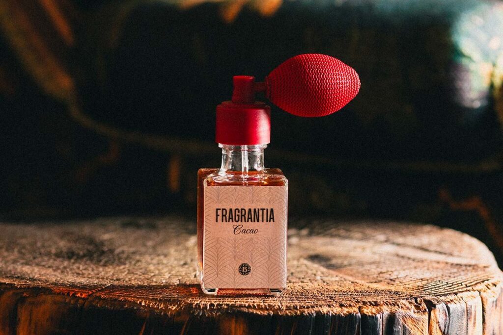 A bottle of Fragrantia with a red spray pump resting on a wooden block, against a dark background