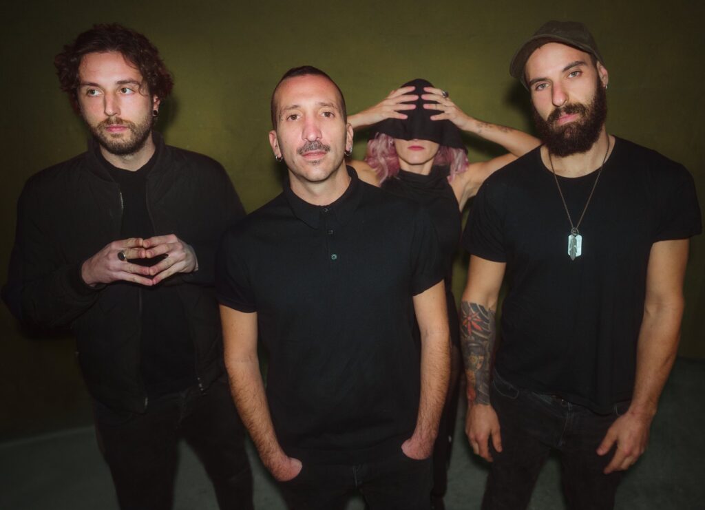 God of the Basement posing in black against an olive-green wall; one member in the back covers his face with his hands
