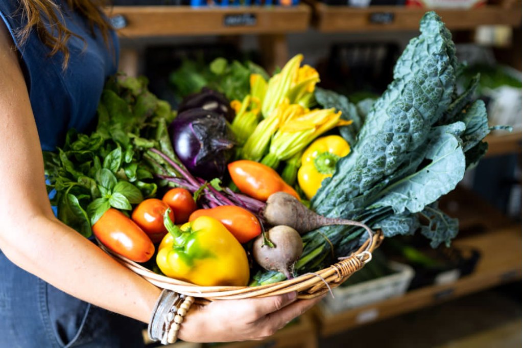 A wicker basket full of tomatoes, peppers, eggplant, zucchini flowers and cavolo nero, held in someone's arms