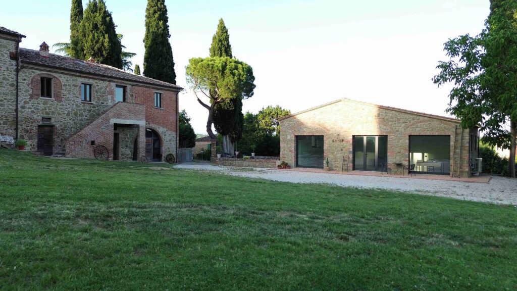 Il podere di La CAP Re|Hub a Sinalunga: casolare in pietra, cipressi e un annesso ristrutturato affacciato su un prato