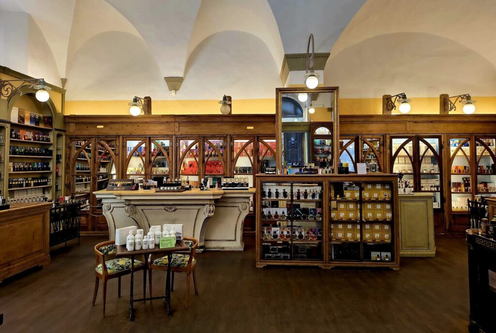 Interior of a perfumery with cross vaults, dark wooden shelves full of bottles, and a counter in the middle