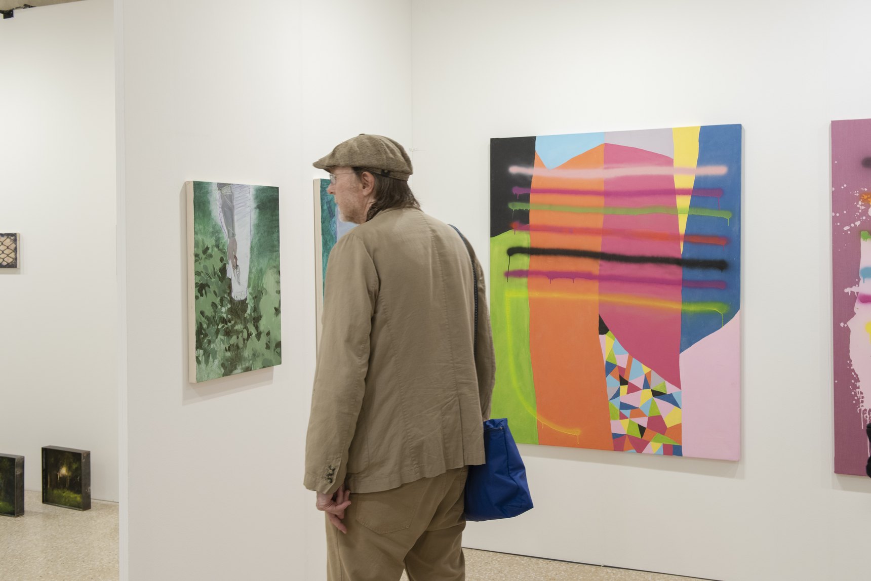 Un visitatore con cappello osserva un grande dipinto astratto dai colori accesi in uno stand della fiera