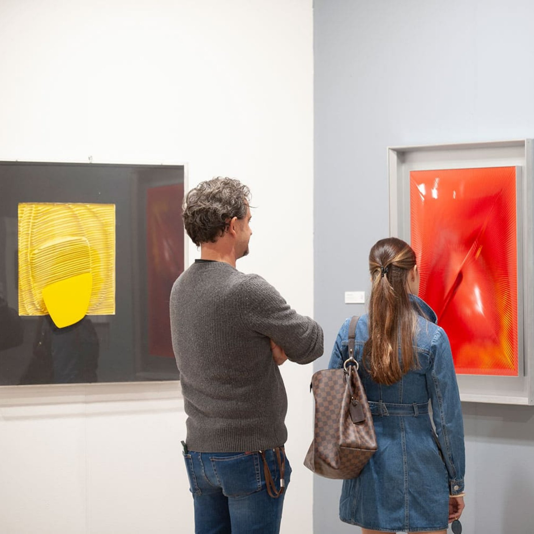 Due visitatori di spalle guardano un monocromo giallo e una grande tela rossa in uno stand della fiera