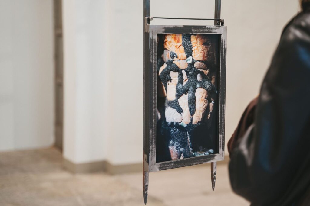 Un'opera verticale sospesa a un'asta metallica in una sala bianca della mostra Bones of Tomorrow di Andro Eradze