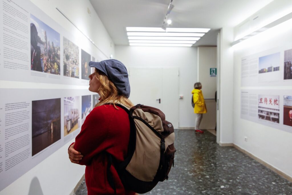 Una visitatrice con zaino e berretto osserva le fotografie appese nel corridoio della mostra The Tilt of Time