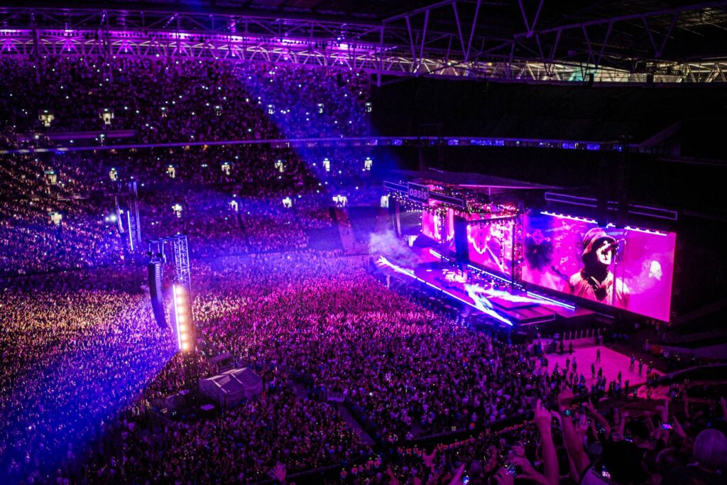 Lo stadio di Wembley pieno di pubblico sotto le luci viola durante il concerto degli Oasis del tour 2025