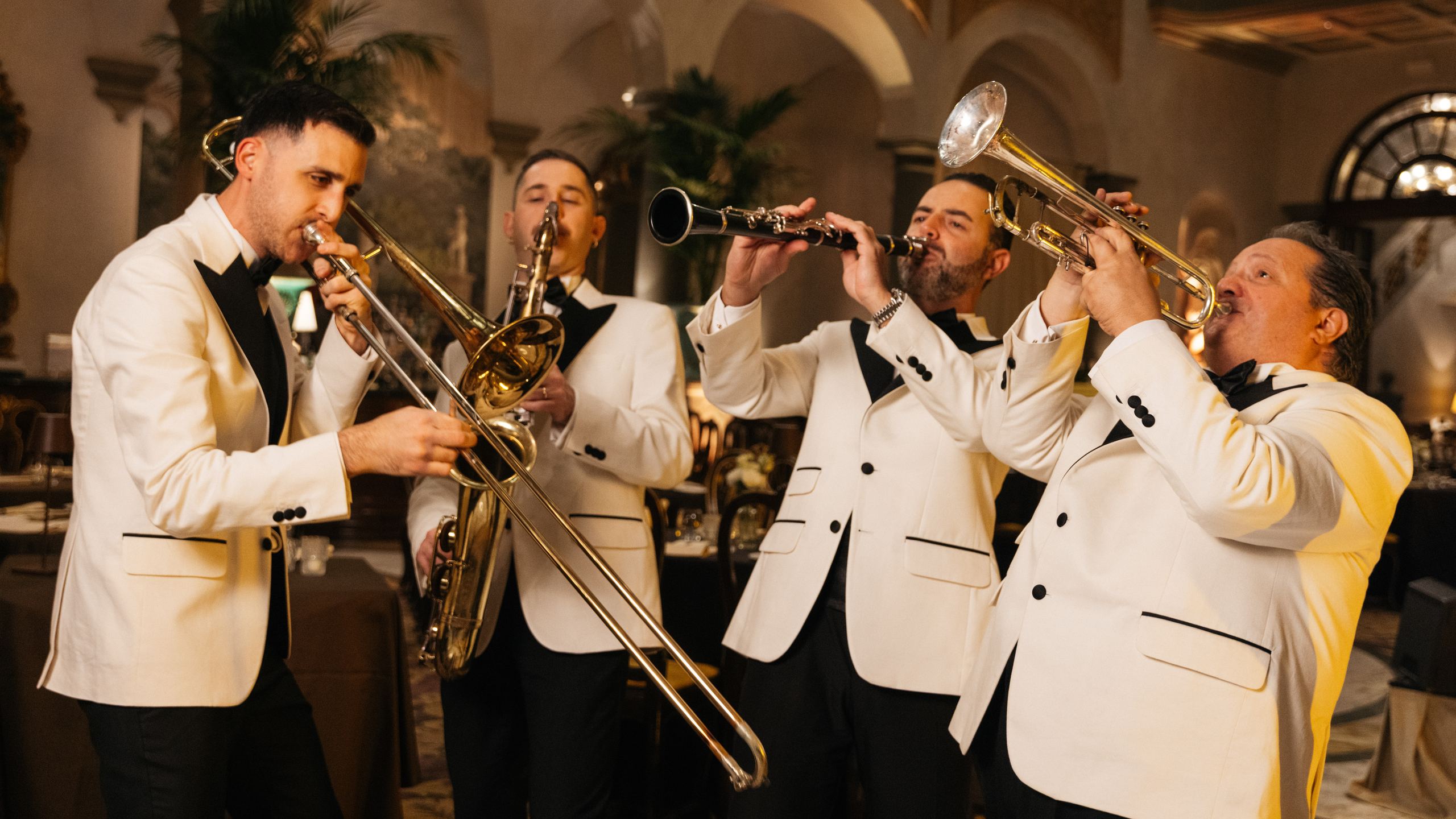 Cinque musicisti in giacca bianca suonano trombone, trombe e clarinetto durante una serata al Winter Garden