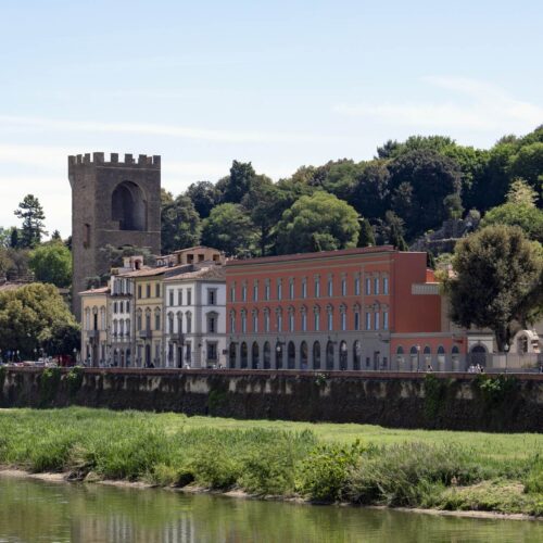 Palazzo San Giorgio visto dall'altra sponda dell'Arno: la facciata rossa sul lungarno, a sinistra una torre medievale