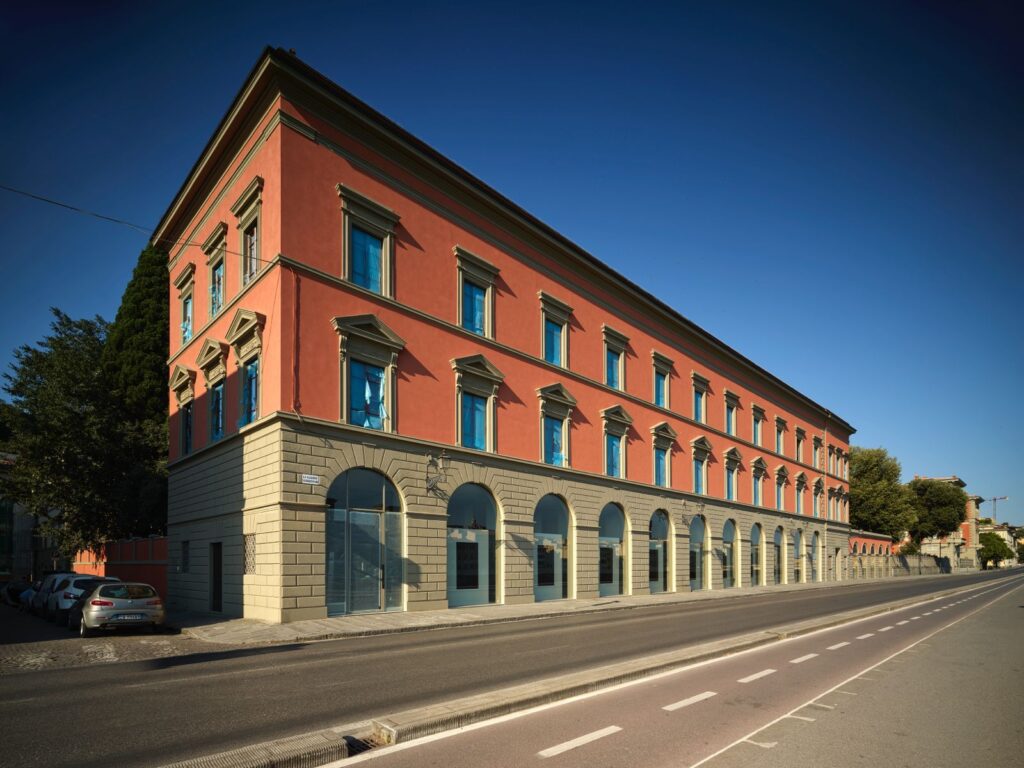 Palazzo San Giorgio visto di scorcio dal Lungarno Serristori, facciata rossa e piano terra ad arcate sotto il cielo blu