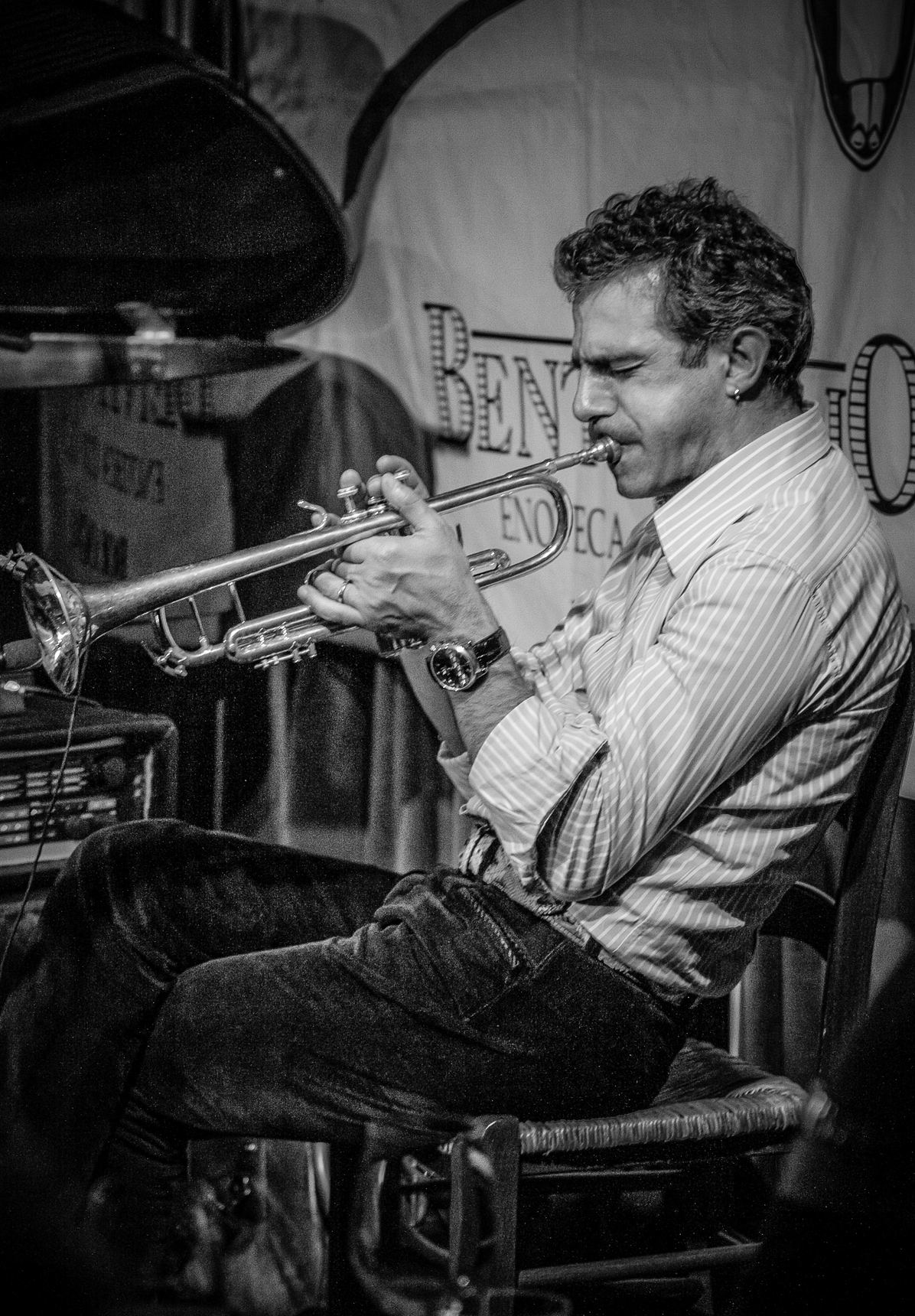 Paolo Fresu, seated, playing the trumpet in a black-and-white photo with a sign behind him