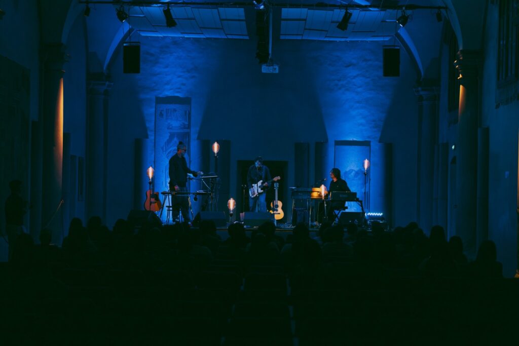 Il palco della Sala Vanni di Firenze illuminato di blu durante un concerto, con il pubblico in controluce