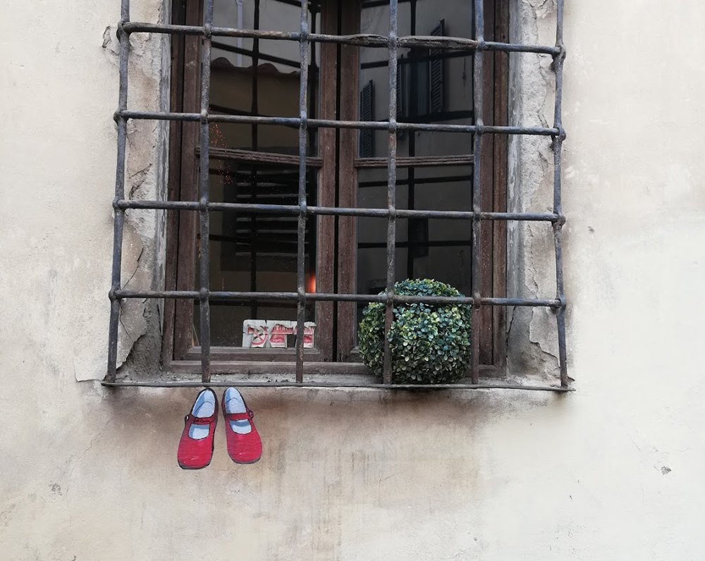 Un paio di scarpe rosse fissate al muro sotto una finestra con l’inferriata, in una strada di Firenze