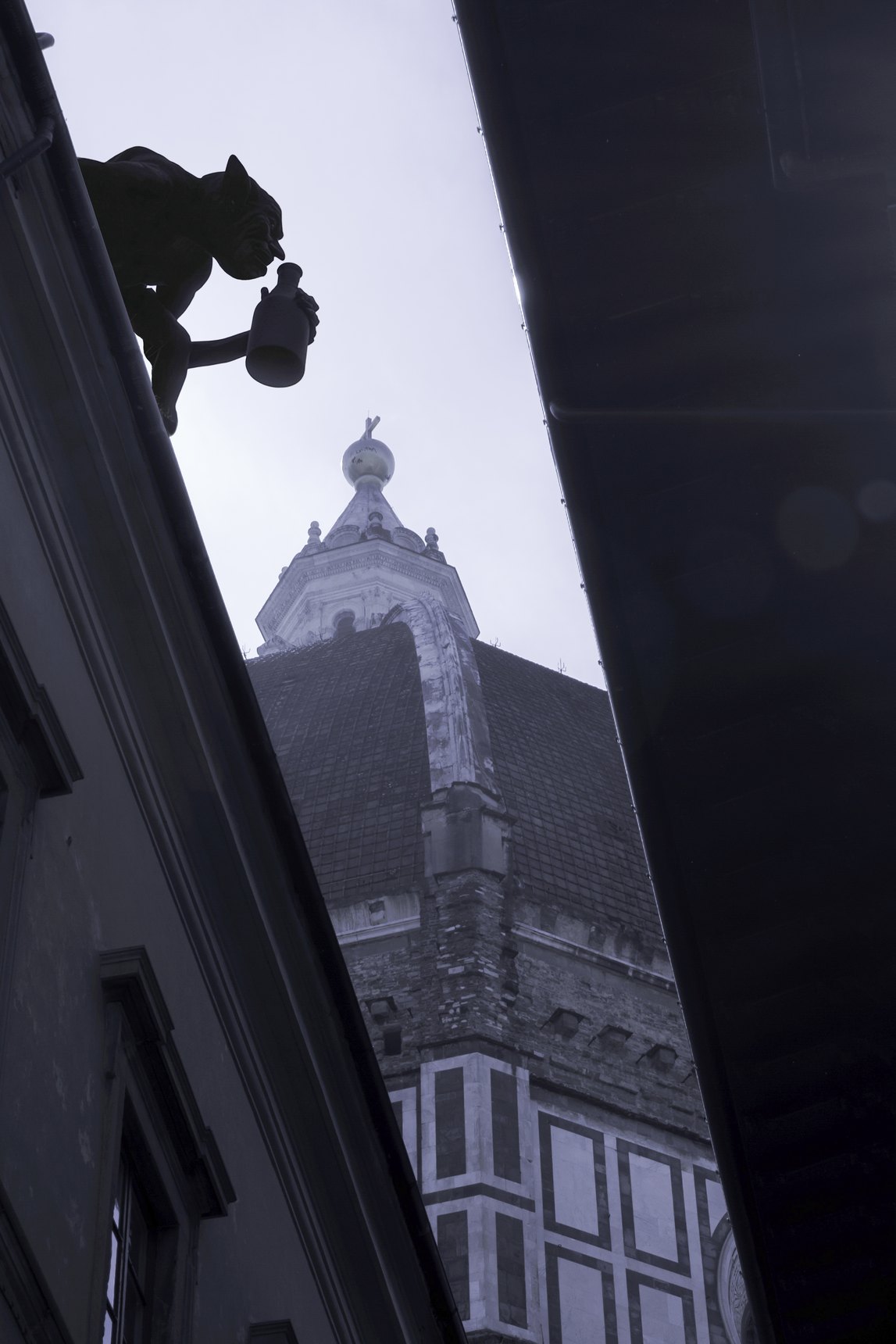 Sagoma di folletto con una brocca sul cornicione di un palazzo, con la lanterna del Duomo di Firenze dietro