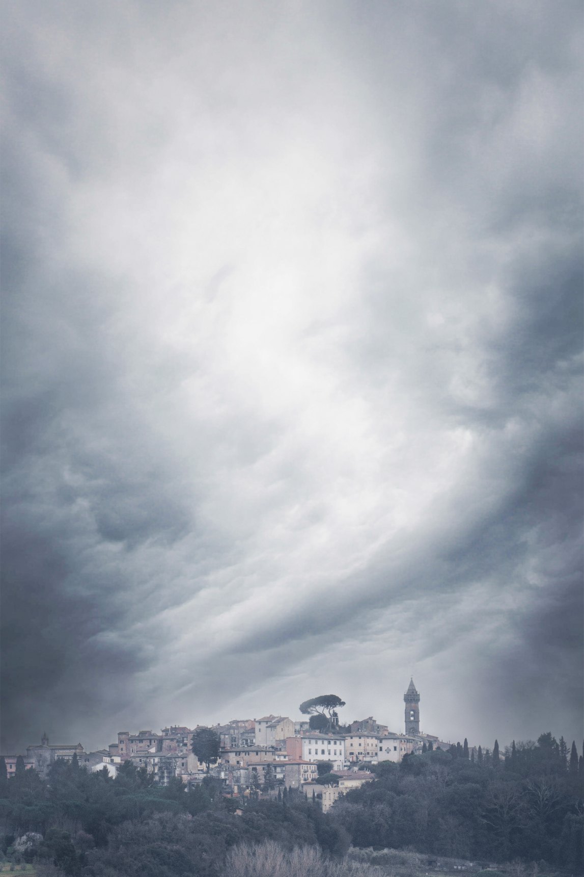 Il borgo di Peccioli sulla collina sotto un cielo di nuvole scure e vorticose, con il campanile in cima