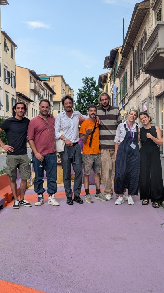 Sette persone in posa sulla pavimentazione dipinta di lilla e arancio di via Pacinotti, a Firenze, fra le case della strada