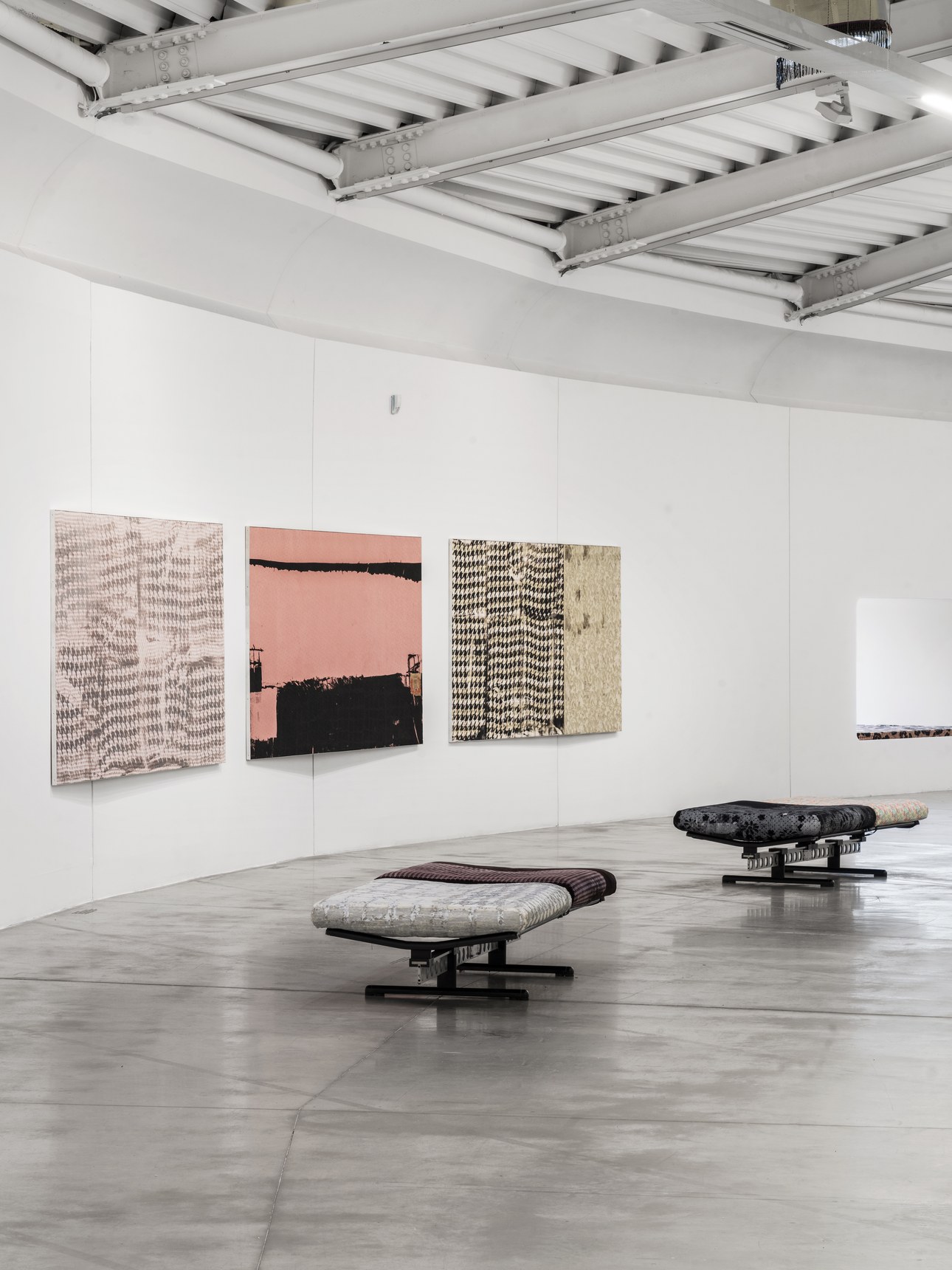 View of the curved room at Centro Pecci with pink and black canvases on the walls and low seating on the floor