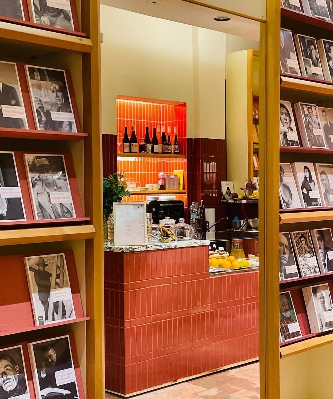 L’angolo bar di Brac & Co. con piastrelle rosse, bottiglie e frutta, fra scaffali di libri illustrati