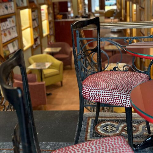 Ringhiera in ferro battuto, sedie e tavolini rossi su un pavimento a mosaico; sotto, la sala della libreria Brac & Co.