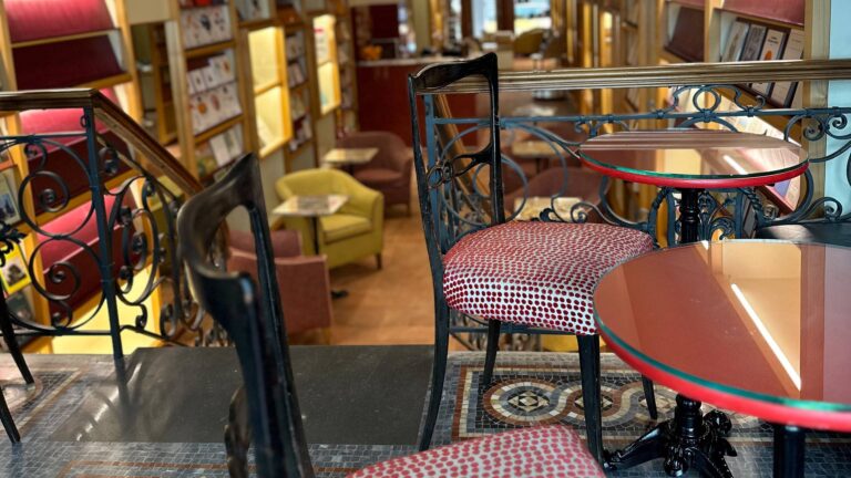 Ringhiera in ferro battuto, sedie e tavolini rossi su un pavimento a mosaico; sotto, la sala della libreria Brac & Co.