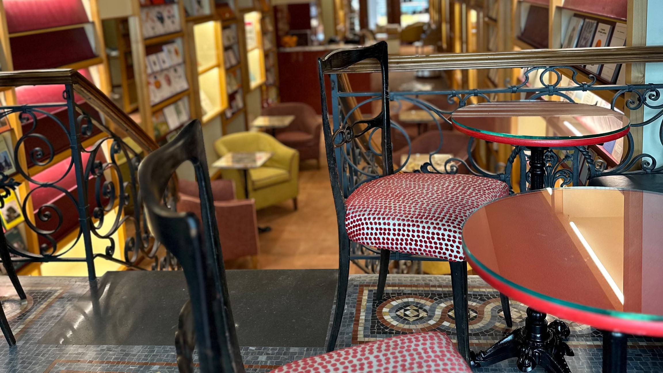 Ringhiera in ferro battuto, sedie e tavolini rossi su un pavimento a mosaico; sotto, la sala della libreria Brac & Co.