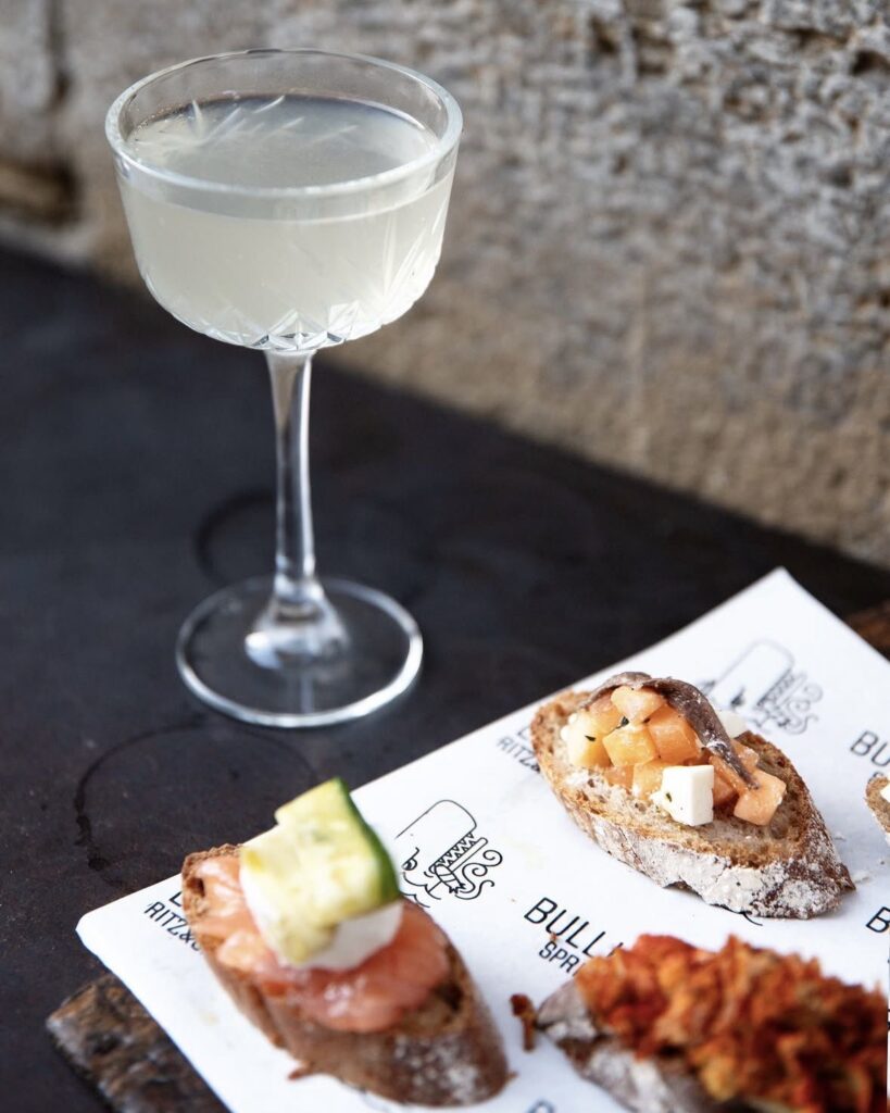 Un cocktail in coppa e cicchetti su pane con salmone e acciughe da Bulli & Balene, alla Manifattura Tabacchi di Firenze