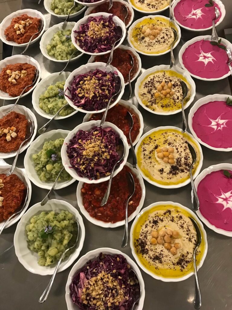 Ciotole bianche di mezè viste dall’alto: hummus, insalate di cavolo viola, salse rosa e rosse con frutta secca