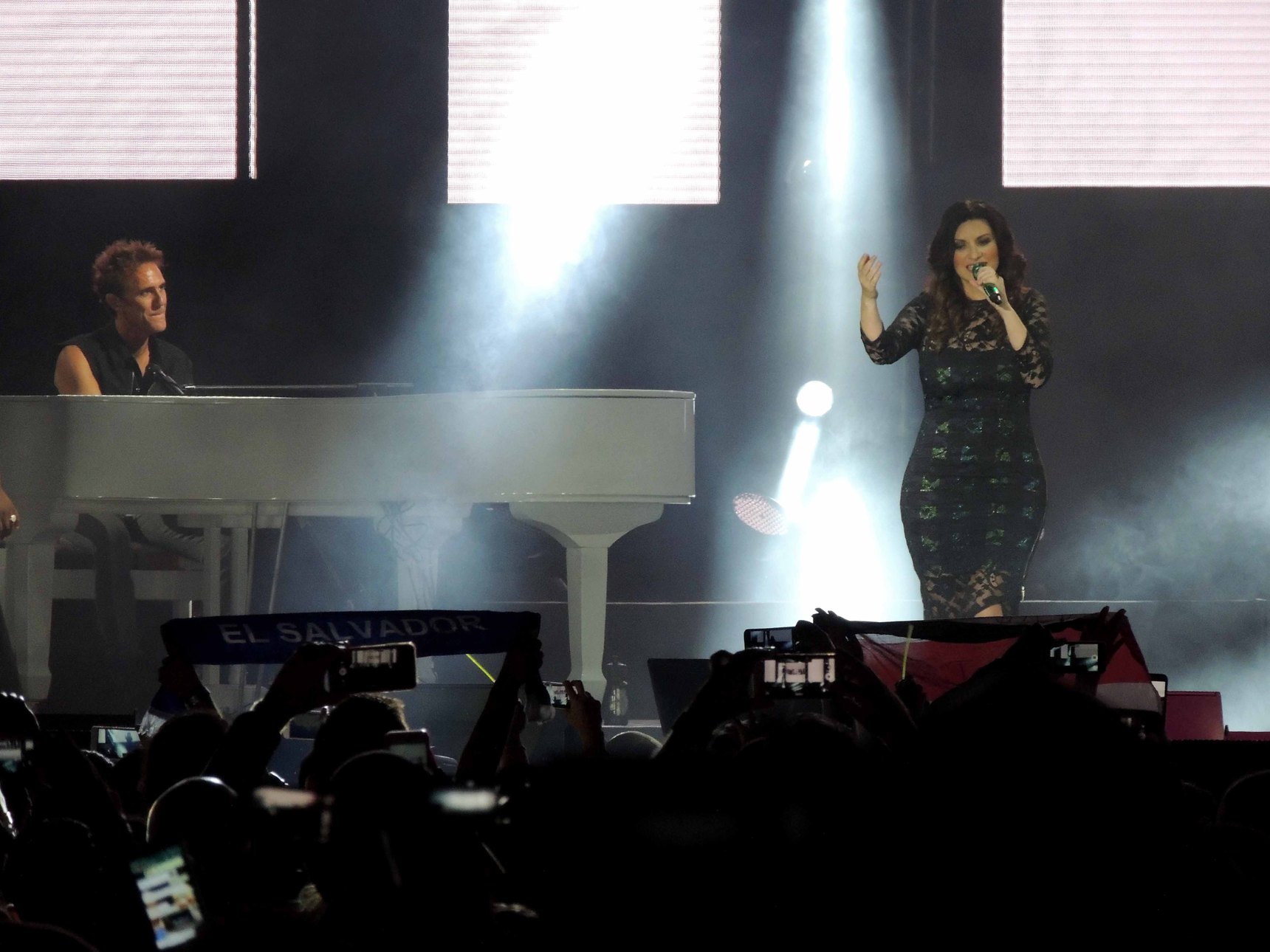Laura Pausini canta su un palco attraversato da fasci di luce bianca, accanto a un pianoforte a coda bianco