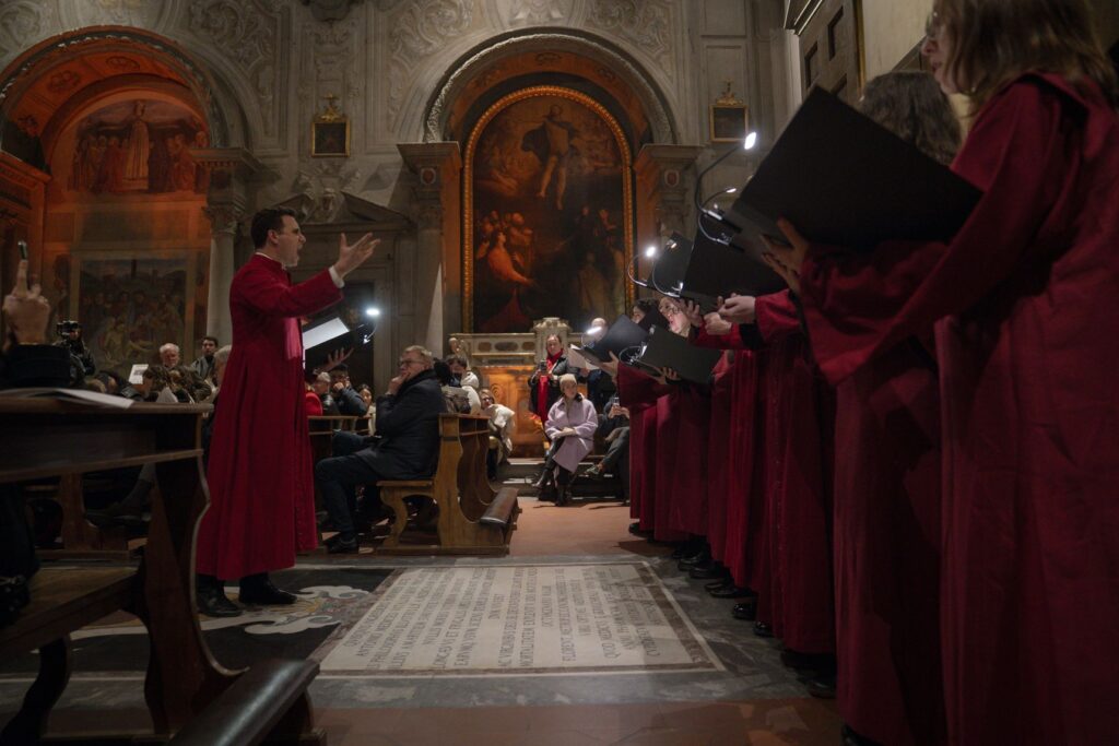 I coristi del Coro di Santo Spirito in tunica rossa cantano in una chiesa di Firenze, davanti a un altare dipinto