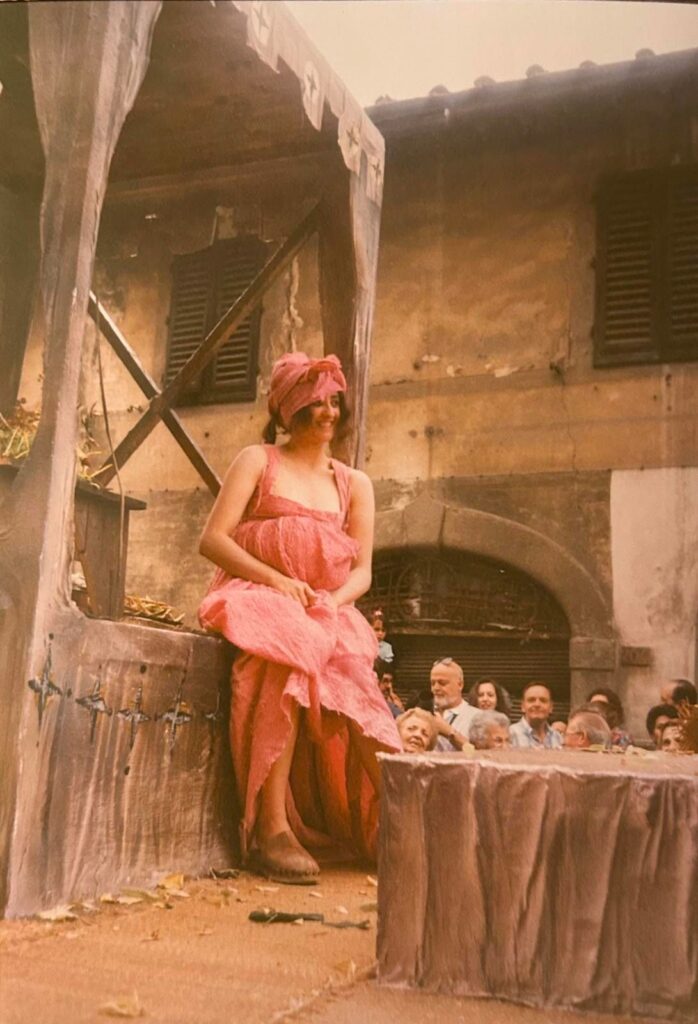 Foto storica di una donna in abito rosa e turbante seduta su un carro scenografico, con il pubblico alle spalle