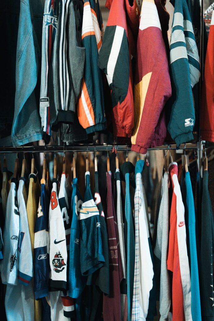 Giacche sportive e maglie da football vintage appese su due file di stender a uno stand di East Market