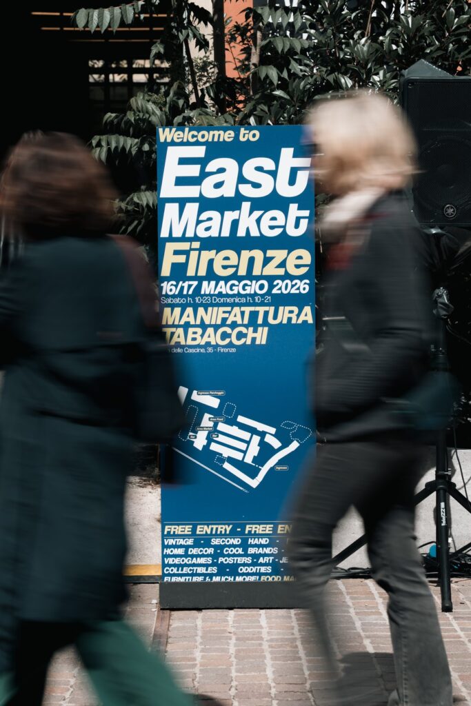 Il totem d'ingresso di East Market Firenze, edizione di maggio 2026, a Manifattura Tabacchi, con due visitatori di passaggio