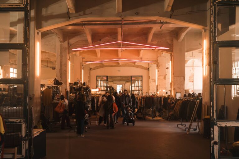 Il padiglione di Manifattura Tabacchi durante East Market: stand di abiti vintage, visitatori e un neon rosa sul soffitto