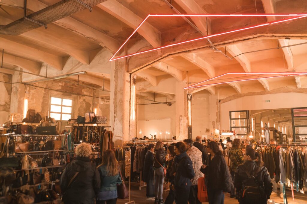 Visitatori tra gli stender di abiti vintage sotto il soffitto di Manifattura Tabacchi durante East Market