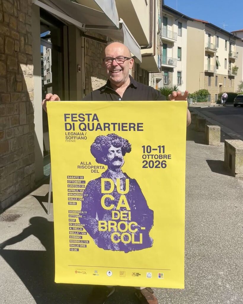 Un uomo sorridente in una strada di quartiere regge il manifesto giallo della festa dedicata al Duca dei Broccoli